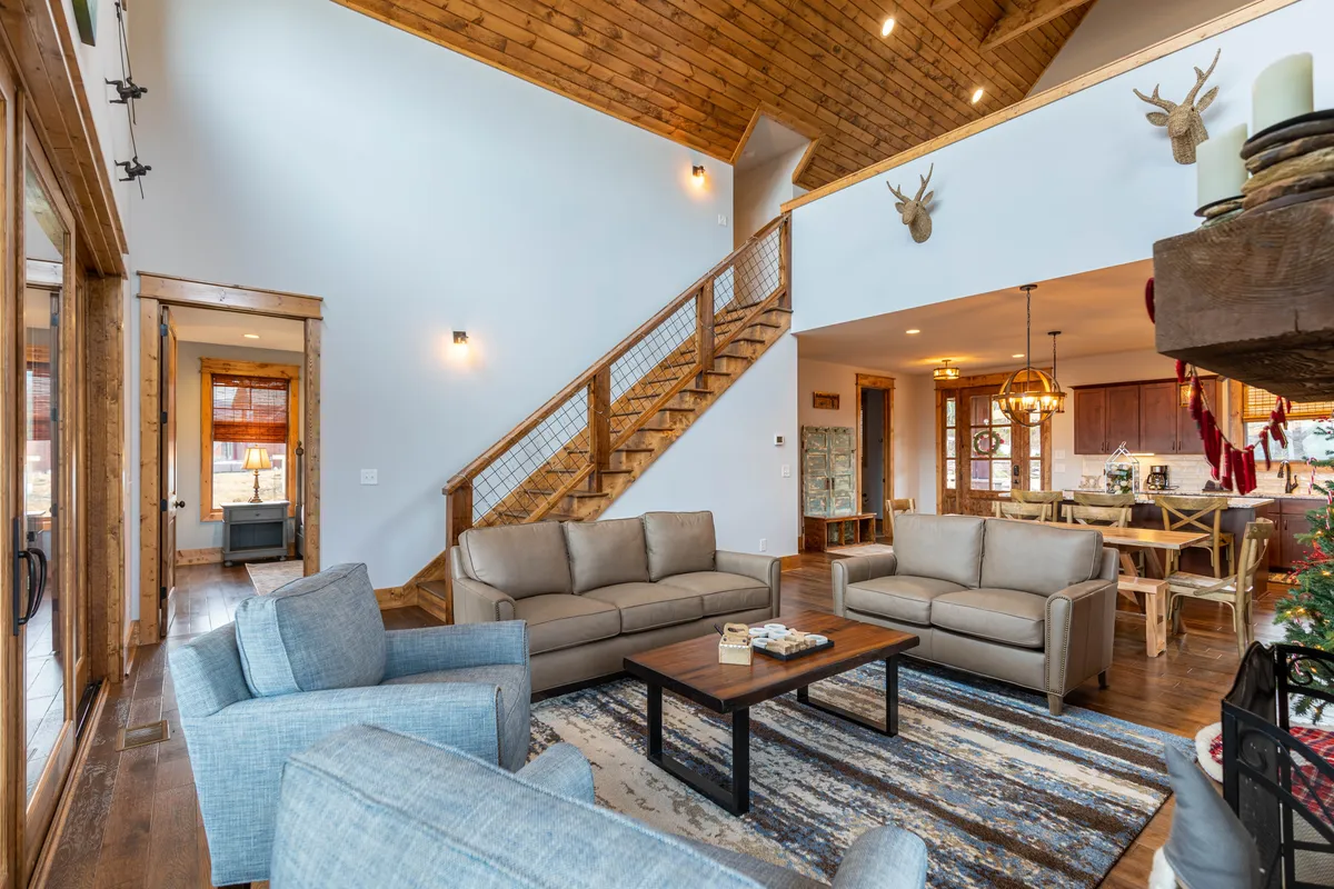 This image features an inviting interior space with a staircase, cozy sofas gathered around a fireplace, and a visible dining area in the background. The setting is designed for family gatherings, casual conversations, and relaxing with loved ones, exuding a warm, communal atmosphere.
