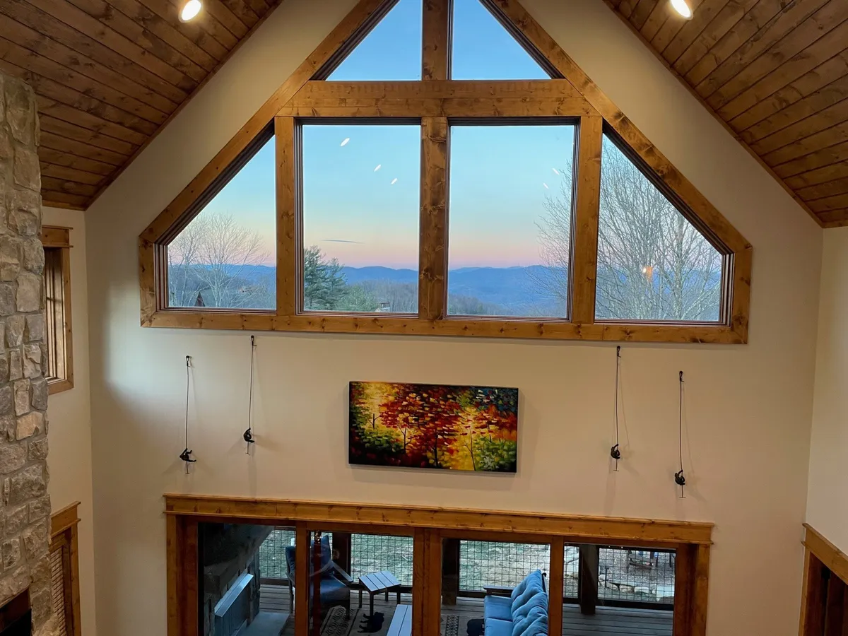 This image features large windows that offer expansive mountain views, complemented by a cozy seating area and colorful wall art. The room is filled with natural light, inviting guests to relax and take in the scenery.