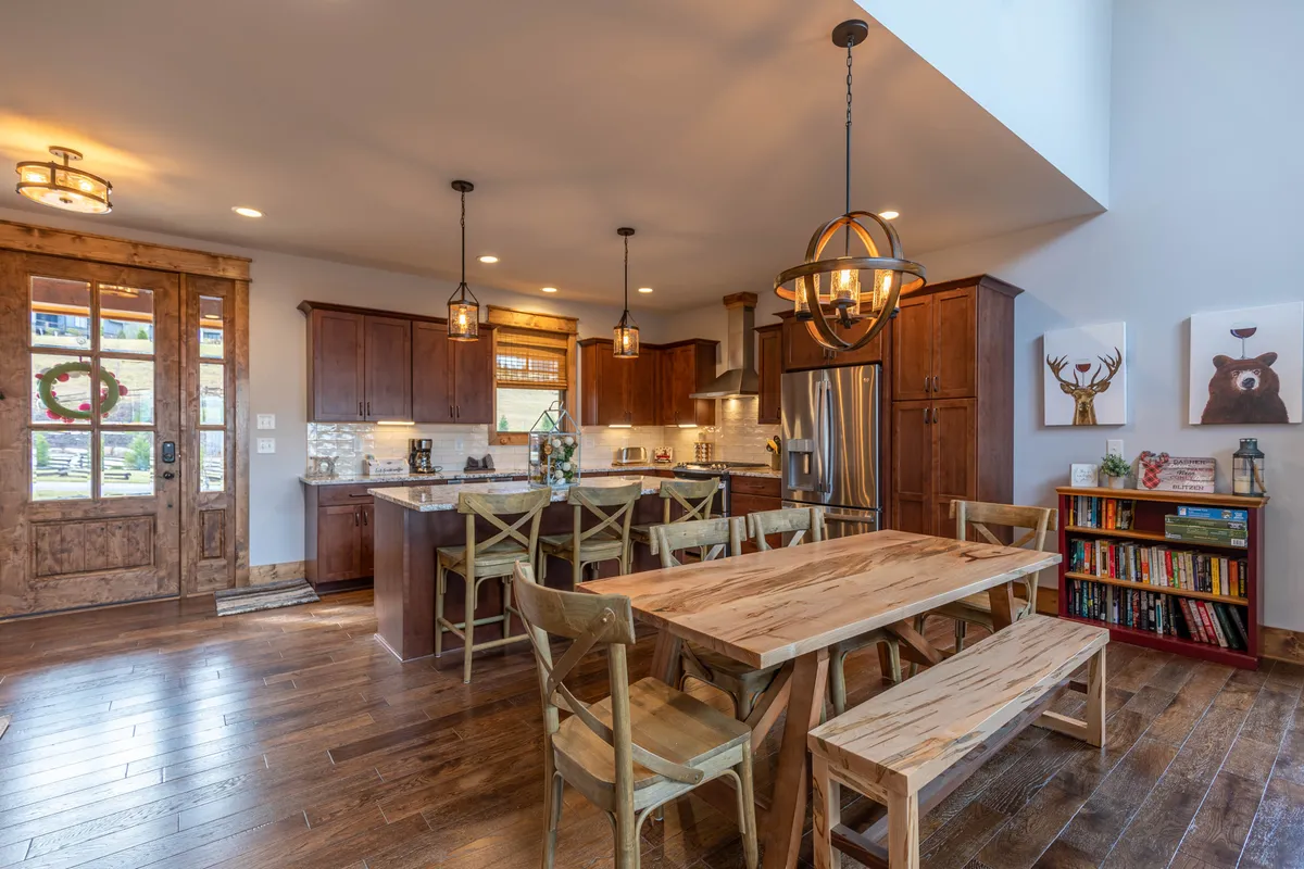 A bright, open dining area featuring a large dining table, adjacent kitchen island, and a rustic wooden door. The space is styled for both everyday family meals and special gatherings, with a cozy atmosphere that encourages togetherness.