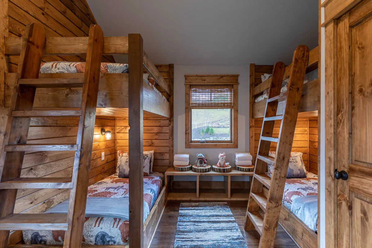A dedicated bunk room featuring charming wooden bunk beds, decorative cushions, and a window view that lets natural light gently brighten the space. The playful yet comfortable environment is clearly designed with children in mind, offering both sleep and play opportunities.