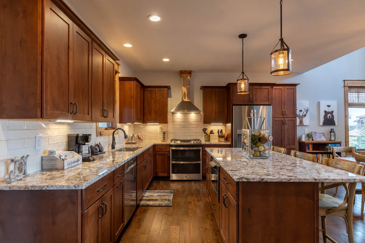 A welcoming kitchen featuring a central island with granite countertops, stainless steel appliances, warm wooden cabinetry, and soft pendant lighting overhead. The space feels open and functional, ideal for preparing meals or gathering with loved ones.