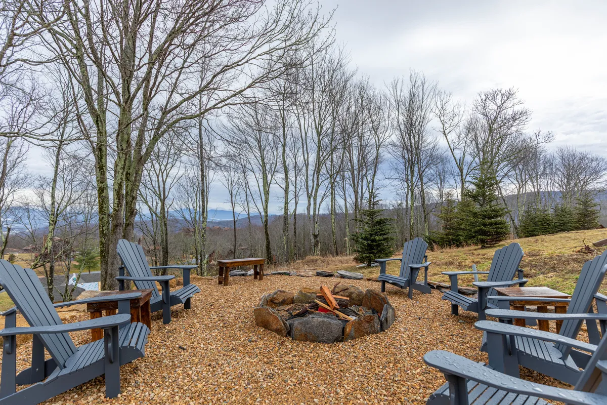 This exterior image displays a classic fire pit encircled by adirondack chairs, nestled amongst trees. The setting evokes warmth, storytelling, and shared moments, inviting guests to gather for campfire meals or stargazing.