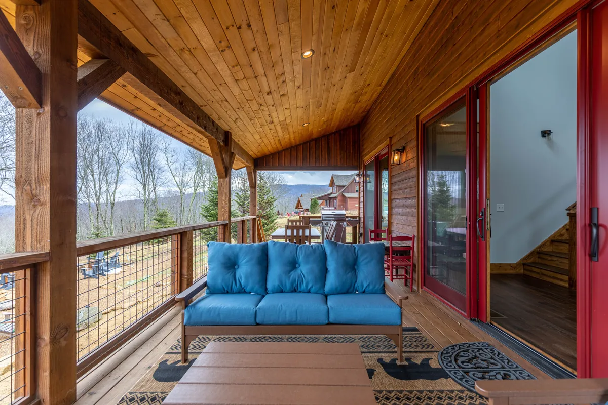 A cozy exterior deck furnished with a blue sofa, bordered by a wooden railing and overlooking stunning mountain views. The setup encourages relaxation, conversation, and appreciating the great outdoors.